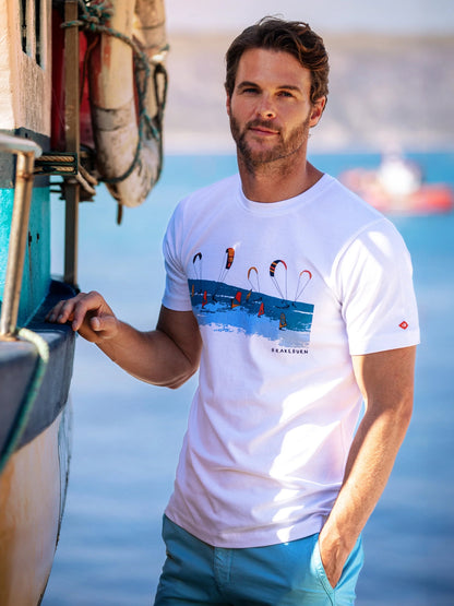 Man wearing a white Brakeburn Watersports print t-shirt, standing near a boat with water in the background