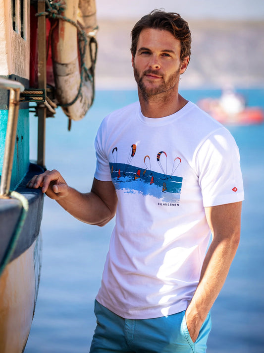 Man wearing a white Brakeburn Watersports print t-shirt, standing near a boat with water in the background