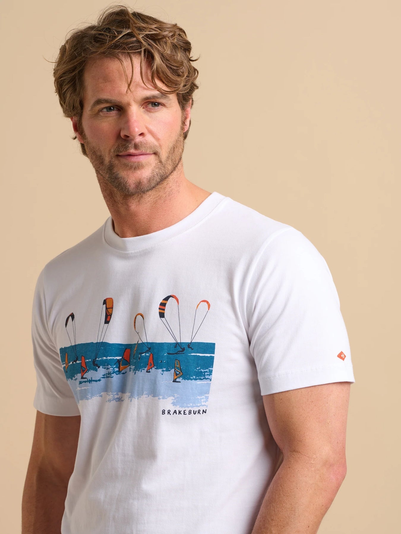 Man wearing a white Brakeburn Watersports t-shirt with a kite and windsurfer print design on a beige background