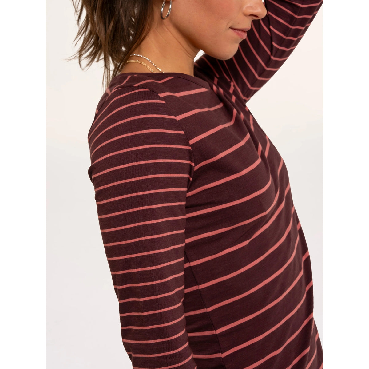 Close-up view of the sleeve of a woman wearing a Brakeburn long sleeve thick and thin stripe Branksome t-shirt in burgundy with coral stripes.
