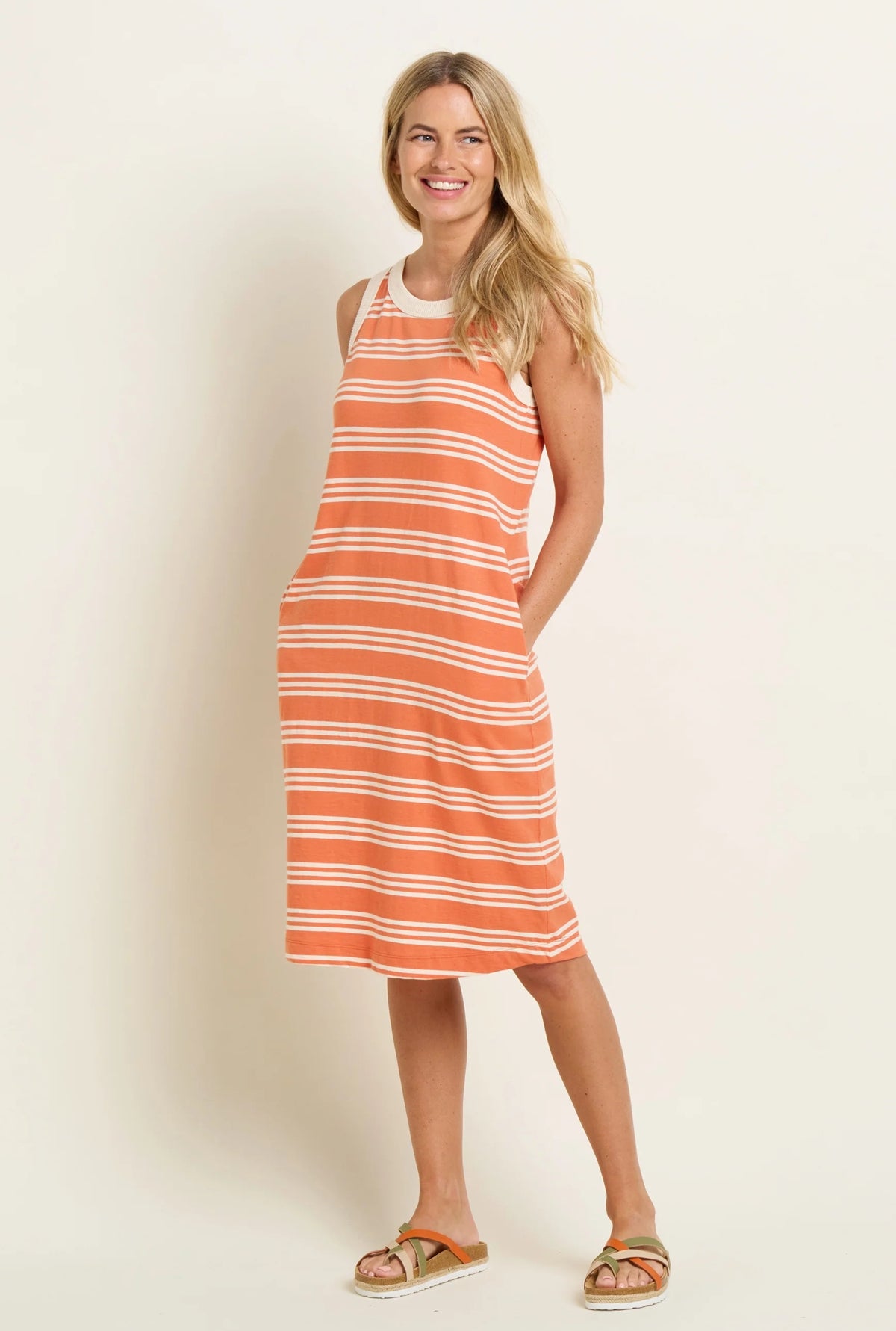 Brakeburn sleeveless stripe dress in orange and white worn by a smiling woman with sandals
