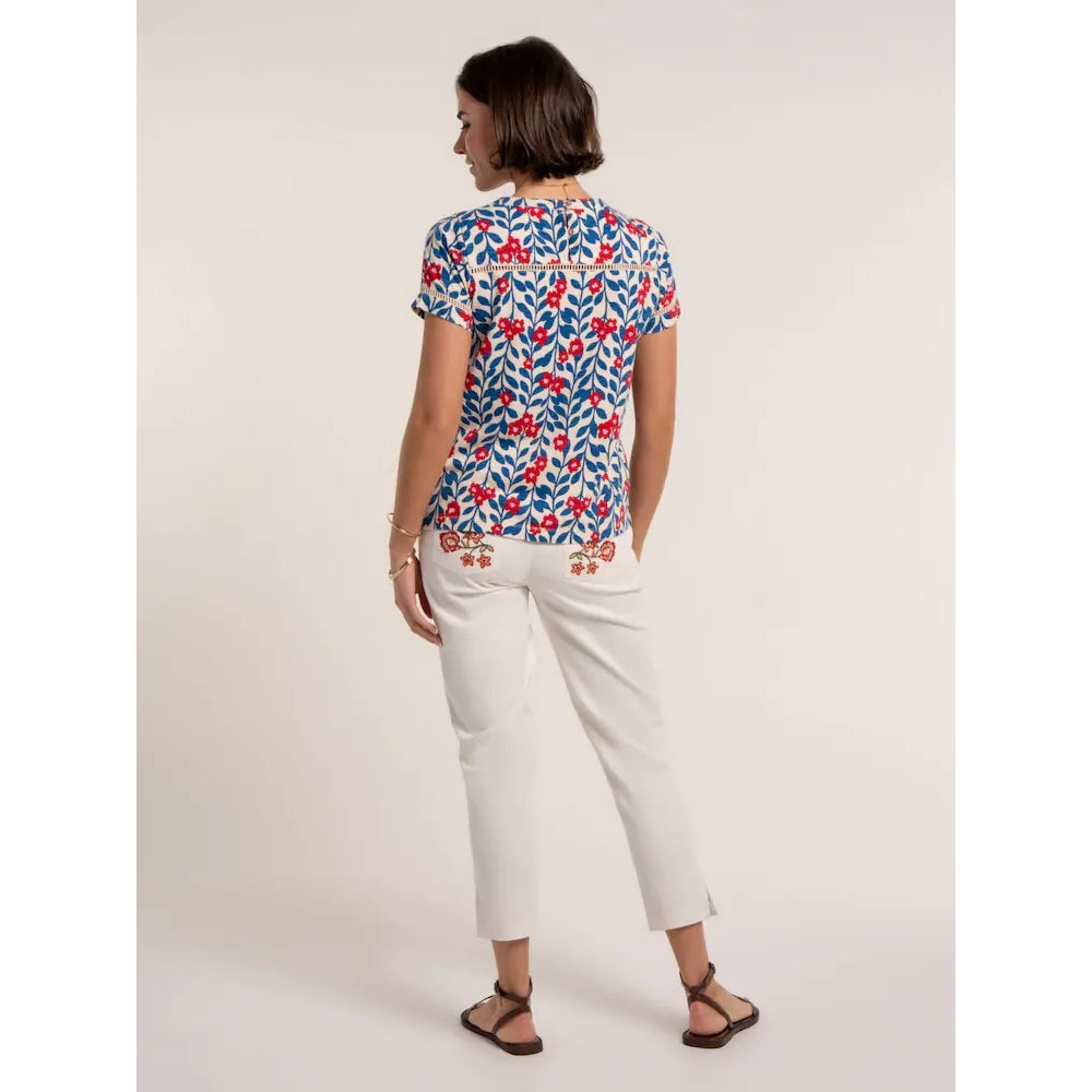 Back view of a woman wearing a Brakeburn short sleeve Clara t-shirt, with a blue and red floral pattern and lace trim with white trousers.