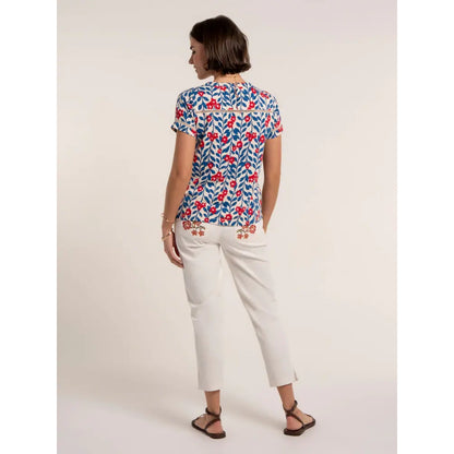 Back view of a woman wearing a Brakeburn short sleeve Clara t-shirt, with a blue and red floral pattern and lace trim with white trousers.