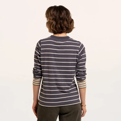 Back view of a woman wearing a Brakeburn long sleeve Exbury t-shirt in light navy with white stripes and contrasting mustard stripe cuffs.