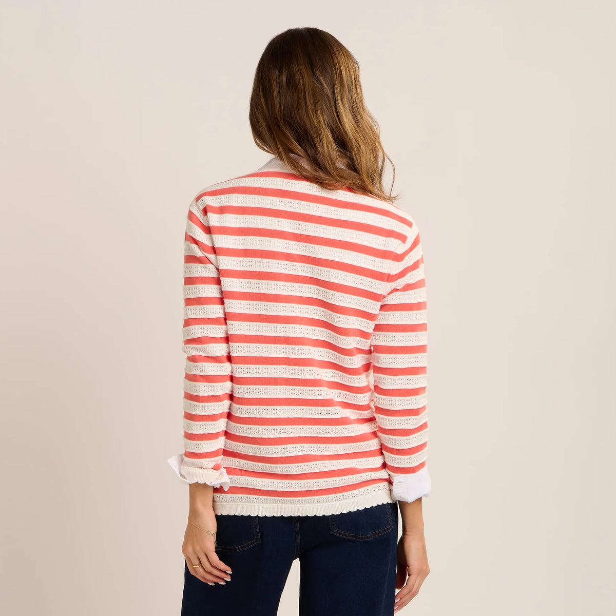 Back view of a woman wearing a Brakeburn Revelle fine knit jumper in coral and white stripe with scalloped detail.
