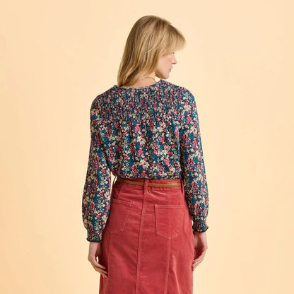 Back view of a woman wearing a Brakeburn Brenda floral long sleeve t-shirt and red skirt on a beige background