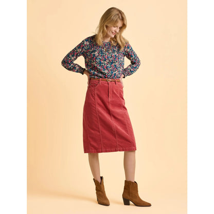 Woman wearing a floral Brakeburn long sleeve floral t-shirt, red skirt, and brown boots on a beige background