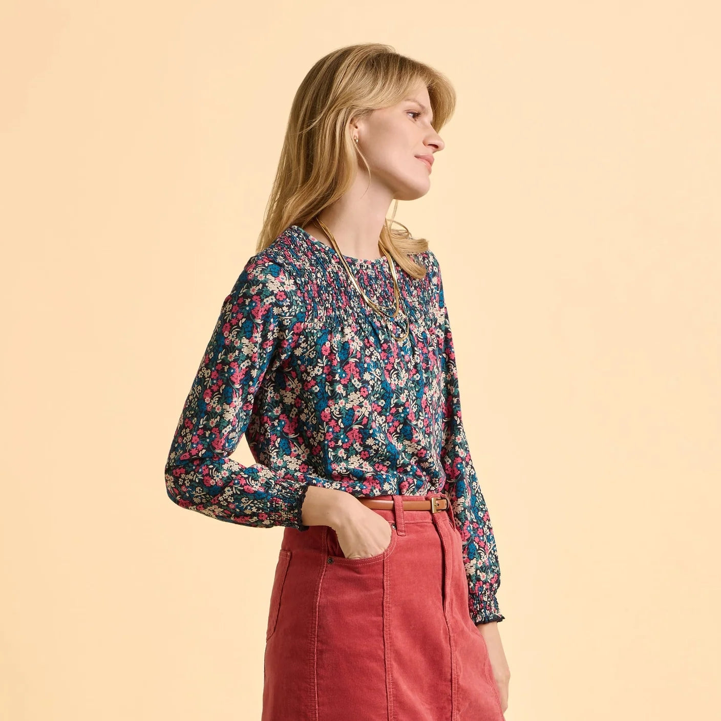 Woman wearing a Brakeburn Brenda floral long sleeve t-shirt and red skirt on a beige background
