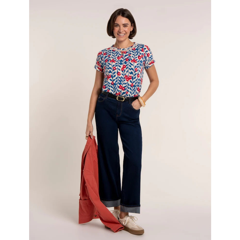 A woman wearing a Brakeburn short sleeve Clara t-shirt with a blue and red floral pattern and lace trim around the neckline and sleeves with navy jeans.