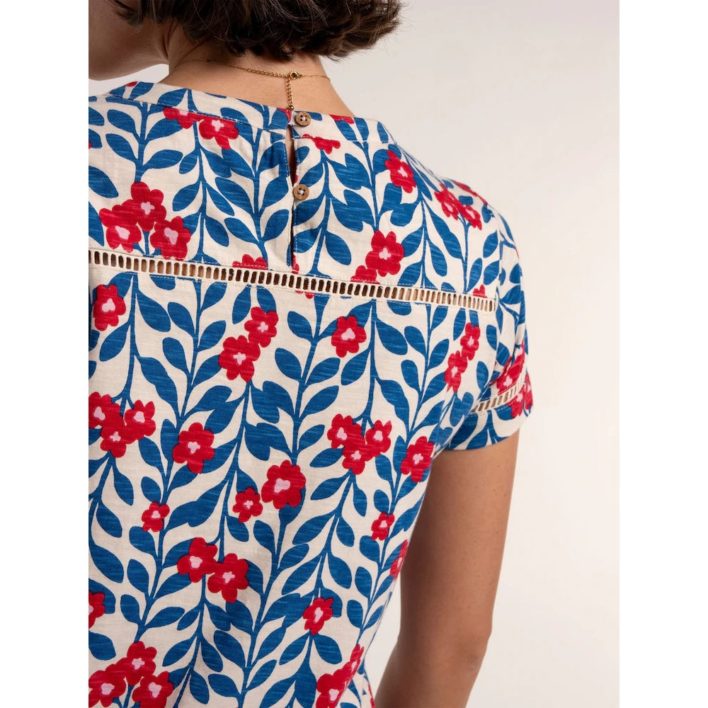 Close-up back view of a woman wearing a Brakeburn short sleeve Clara t-shirt, with a blue and red floral pattern and lace trim across the shoulder and two wooden buttons on the back.