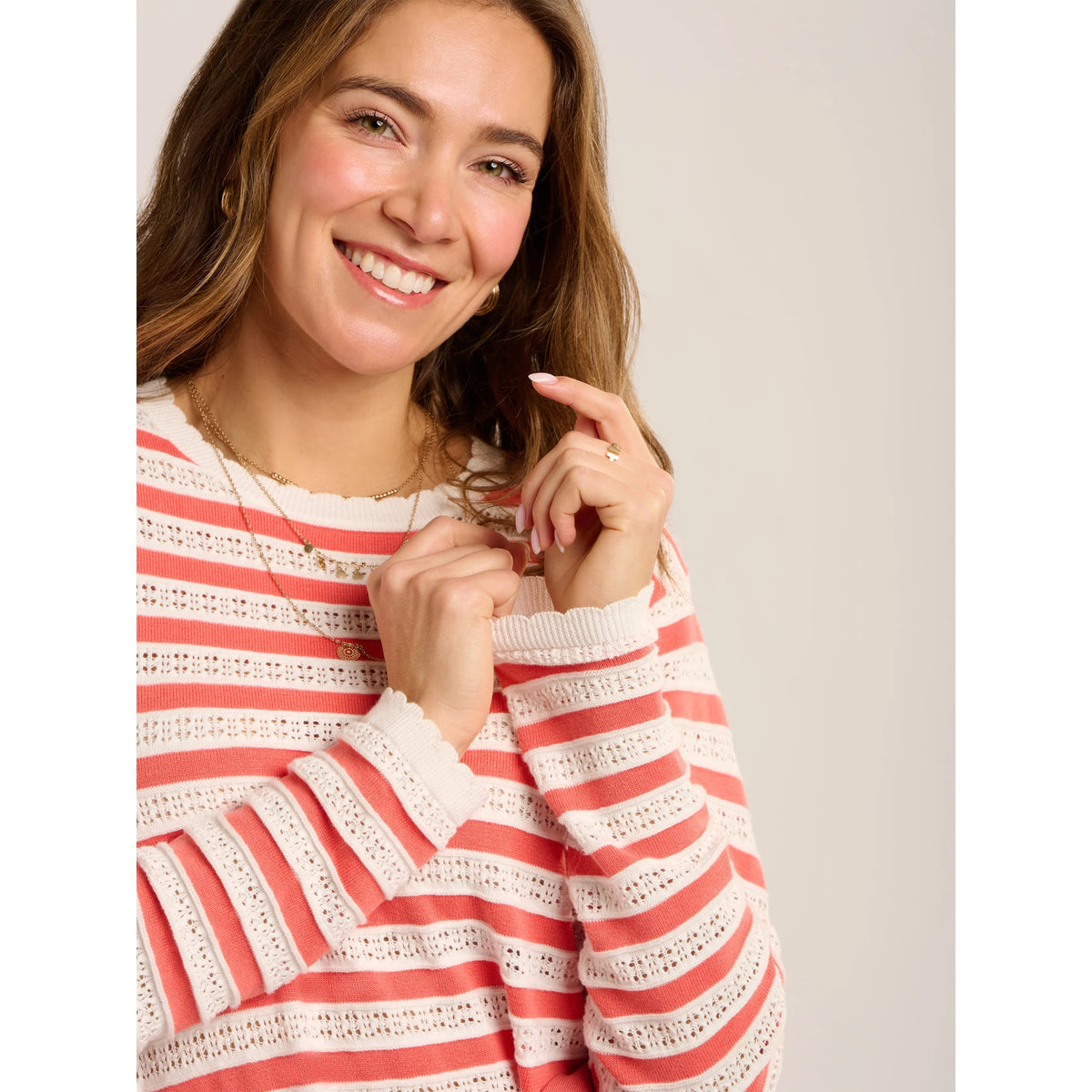 Close-up view of a woman wearing a Brakeburn Revelle textured fine knit jumper in coral and white stripe with scalloped detail.