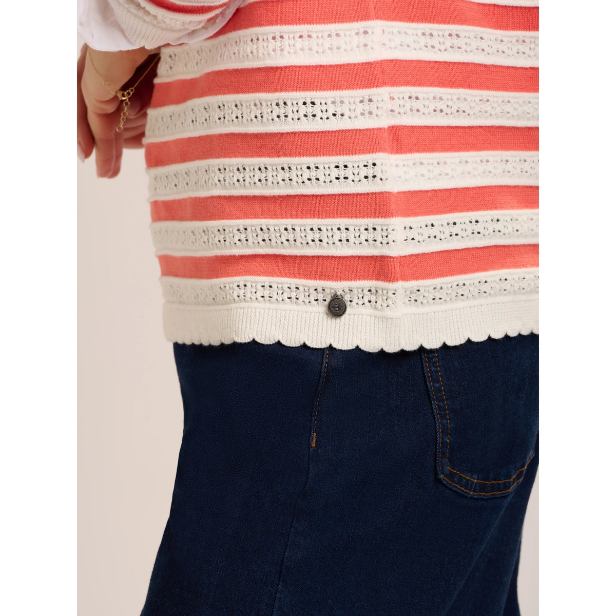 Close-up view of the bottom hem of a woman wearing a Brakeburn Revelle textured fine knit jumper in coral and white stripe with scalloped detail.