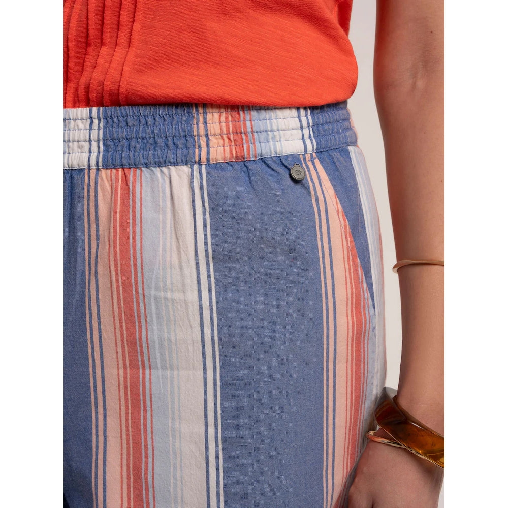 Close-up view of the metal logo fob on a pair of women's Brakeburn Constanza beach shorts in a blue and coral vertical stripe pattern with an elastic waist.
