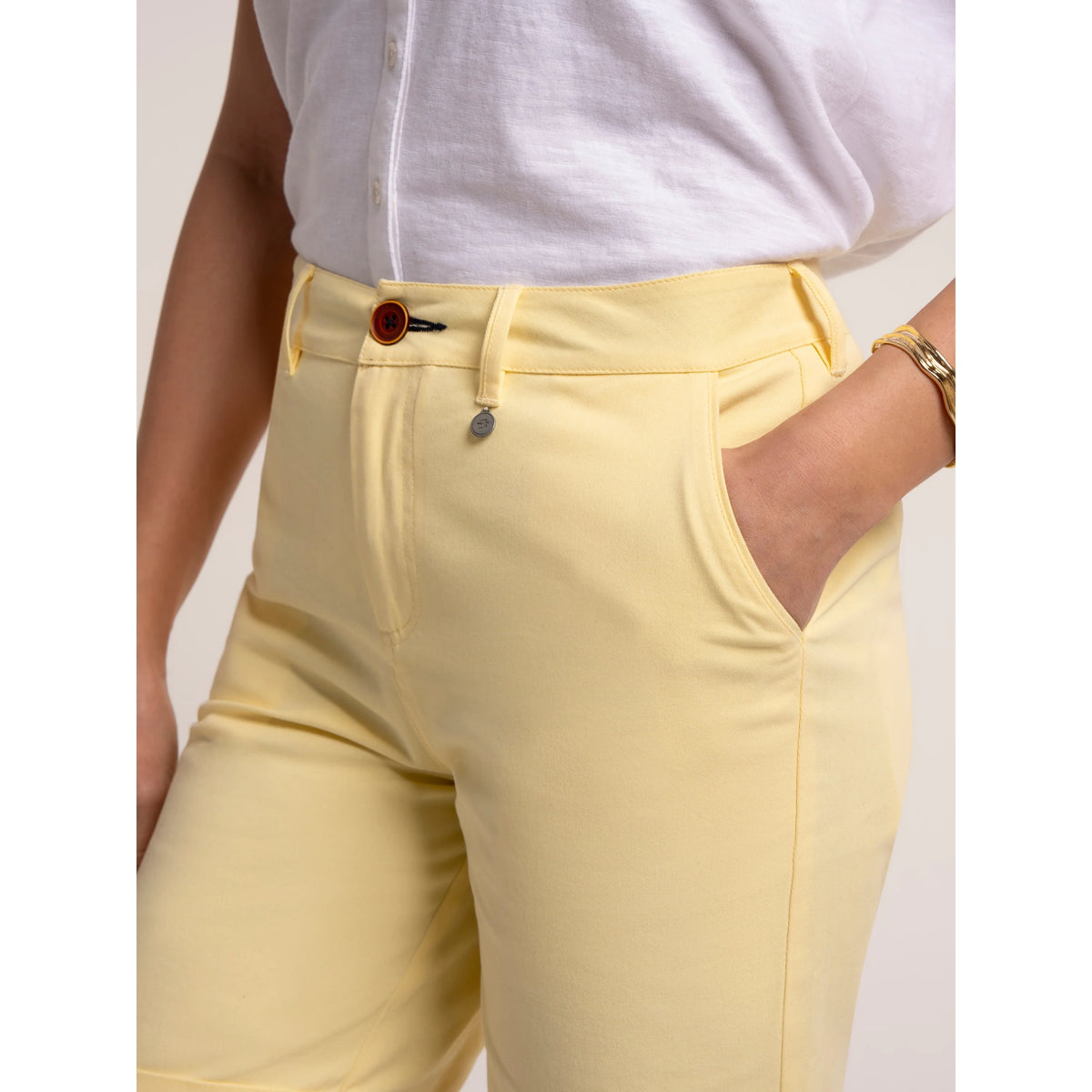 Close-up view of a woman wearing a pair of Brakeburn chino shorts in a soft yellow shade with zip and button fastening, belt loops and hip pockets.
