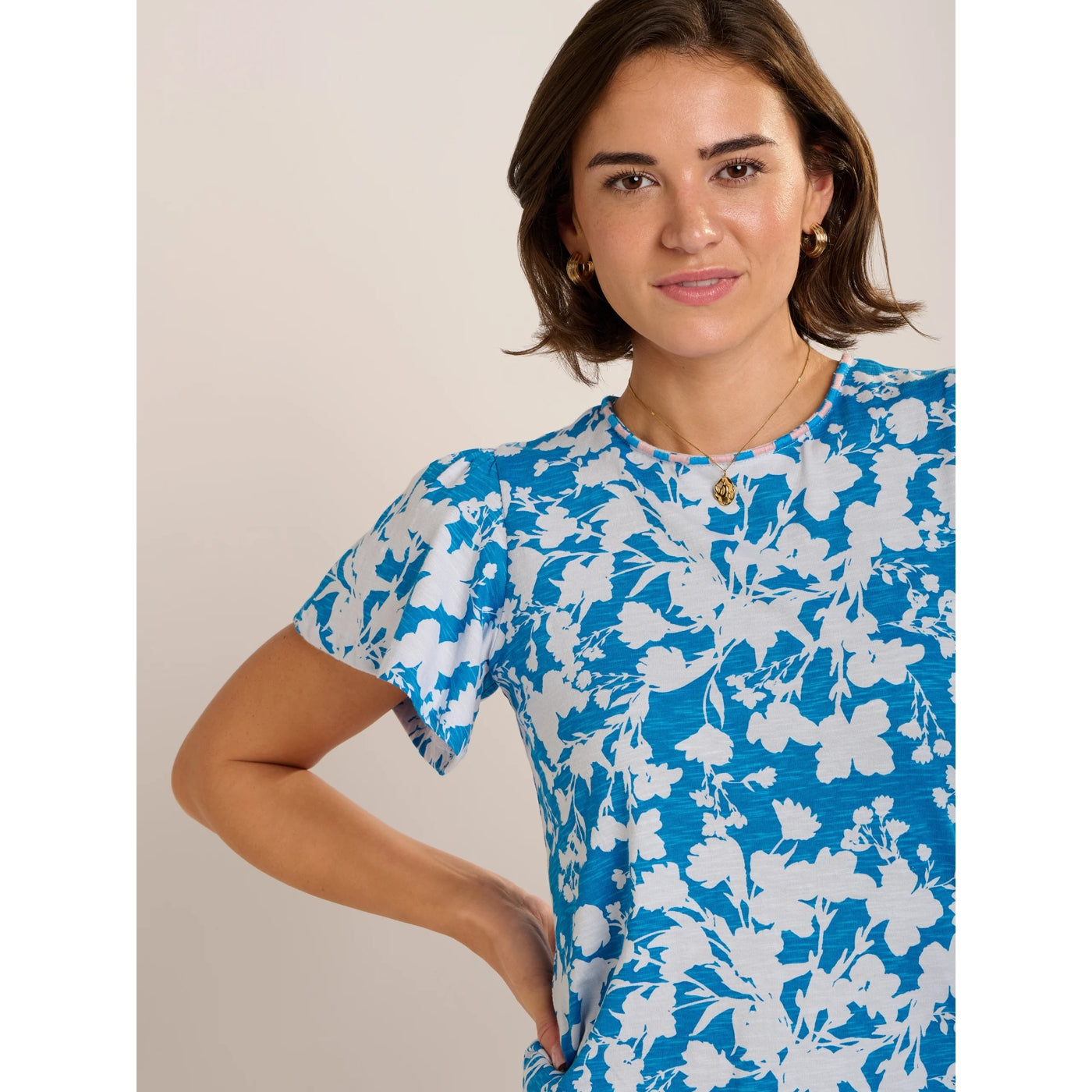 Close-up view of a woman wearing a Brakeburn short sleeve Ria blouse in blue with a white floral print and pink and blue stripe neckline.