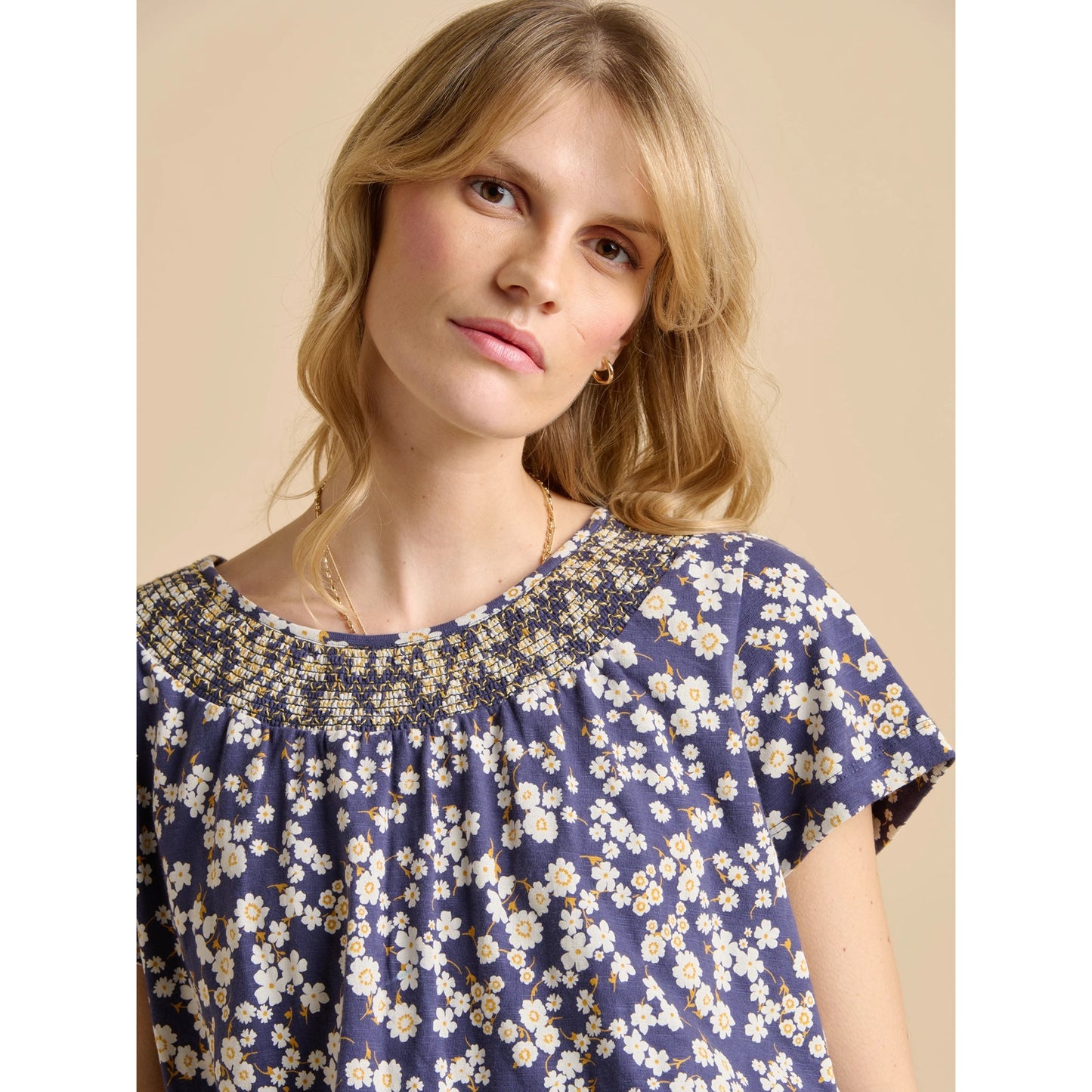 Woman wearing a Brakeburn Floating Daisy T-shirt in navy with a white floral pattern and elasticated neckline, against a beige background