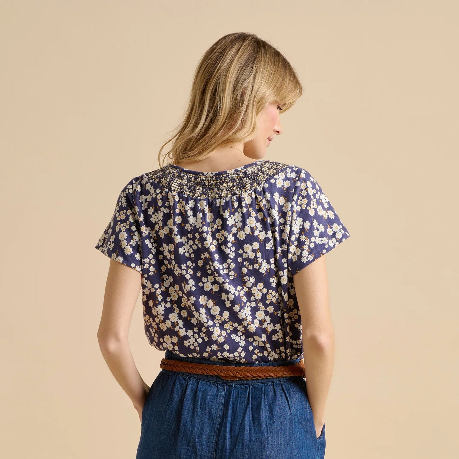 Back view of a woman wearing a Brakeburn short sleeve Floating Daisy T-shirt in a navy and white floral print on a beige background