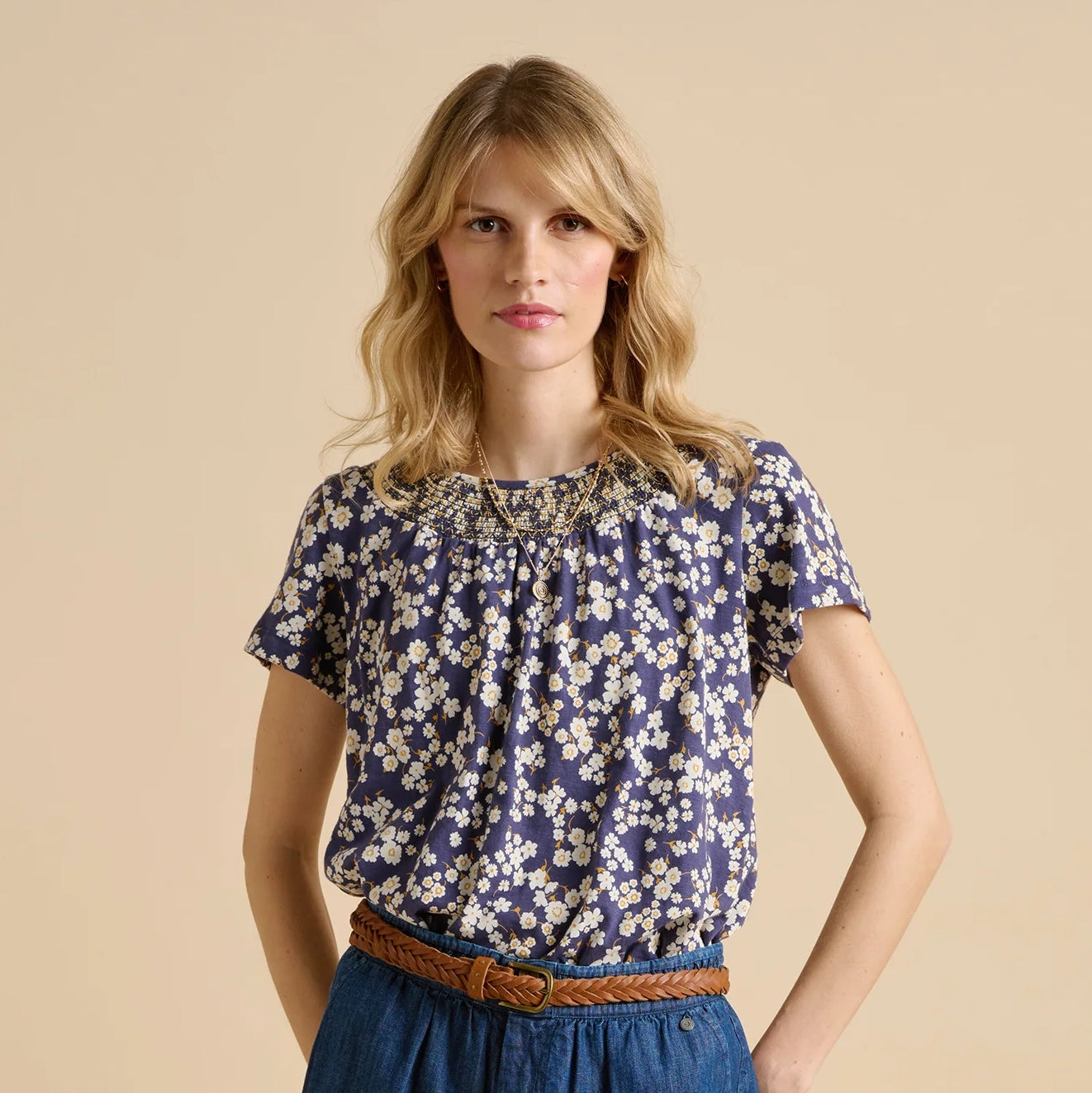 Front view of a woman wearing a Brakeburn short sleeve Floating Daisy T-shirt in navy with a white floral pattern on a beige background