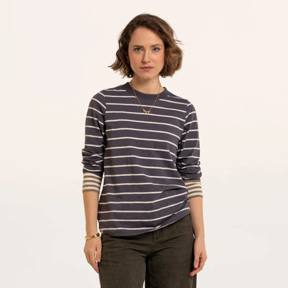 Front view of a woman wearing a Brakeburn long sleeve Exbury t-shirt in light navy with white stripes and contrasting mustard stripe cuffs with dark jeans.