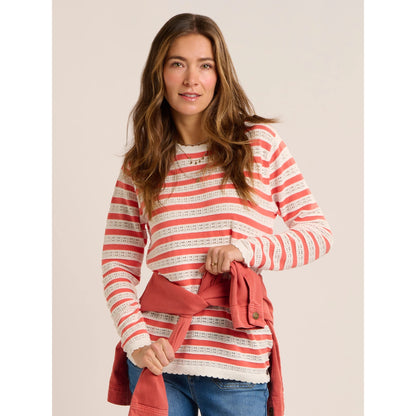 A woman wearing a Brakeburn Revelle fine knit jumper in coral and white stripe with scalloped detail.