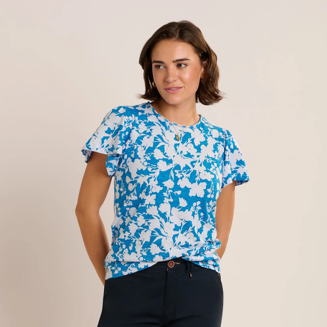 Front view of a woman wearing a Brakeburn short sleeve Ria blouse in blue with a white floral print with navy shorts.