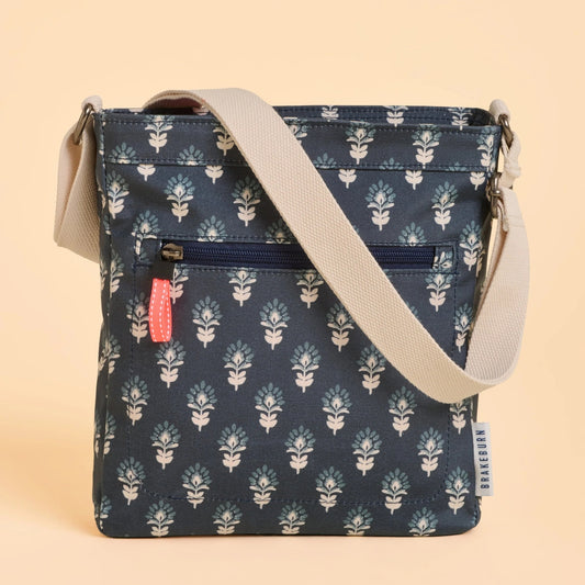 Front view of a Brakeburn Henna floral patterned cross body bag in navy with a beige strap on a beige background