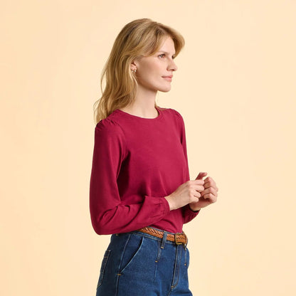 Side view of a woman wearing a red Brakeburn long sleeve Janis t-shirt and blue jeans on a beige background