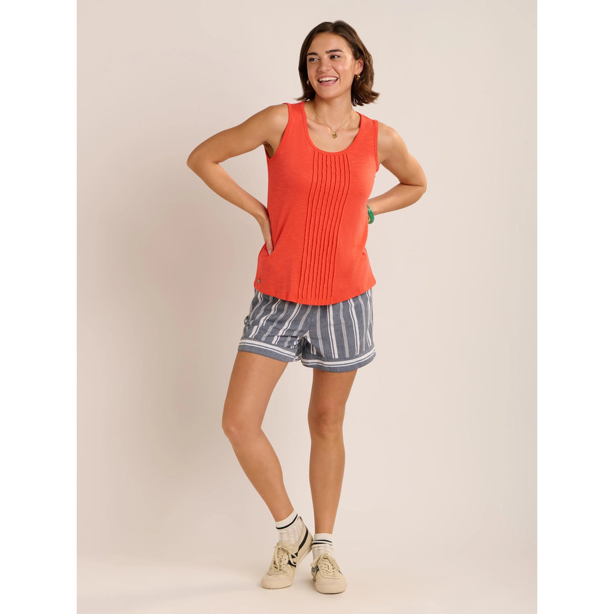 Front view of a woman wearing a pair of Brakeburn loose fit Lettie beach shorts in Navy with a white vertical stripe pattern with an elastic waist, paired with an orange vest.