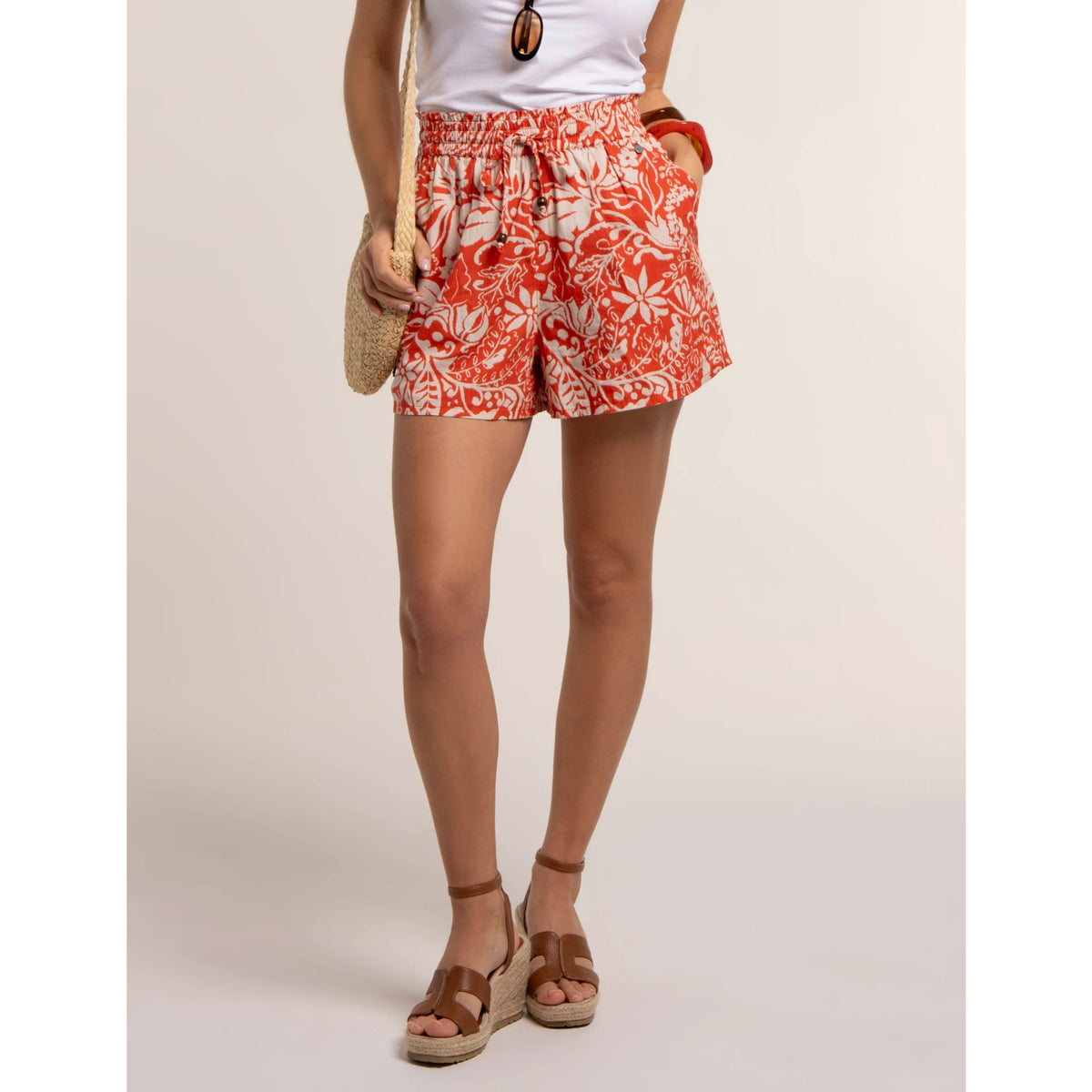 Main front view of a woman wearing a pair of Brakeburn loose fit Bonnie Beach Shorts in coral with a cream floral pattern and elasticated waist.