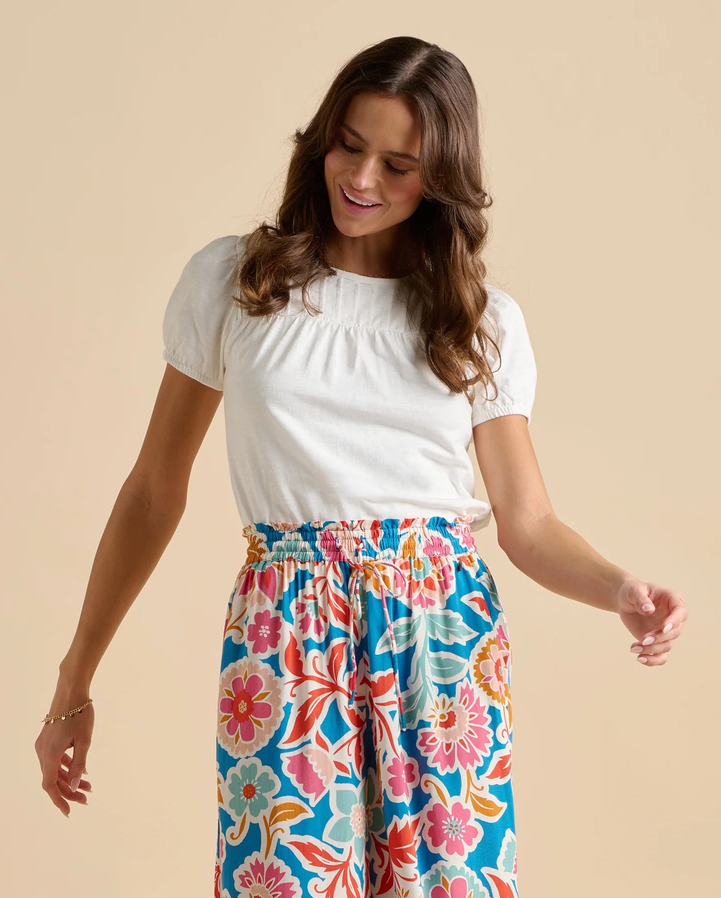 A woman wearing a Brakeburn short sleeve Suri blouse with multicoloured floral trousers on a beige background
