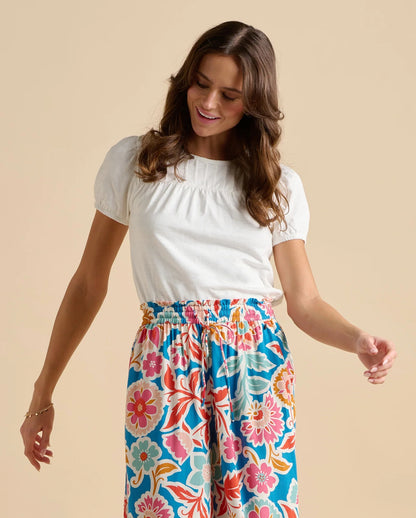 A woman wearing a Brakeburn short sleeve Suri blouse with multicoloured floral trousers on a beige background