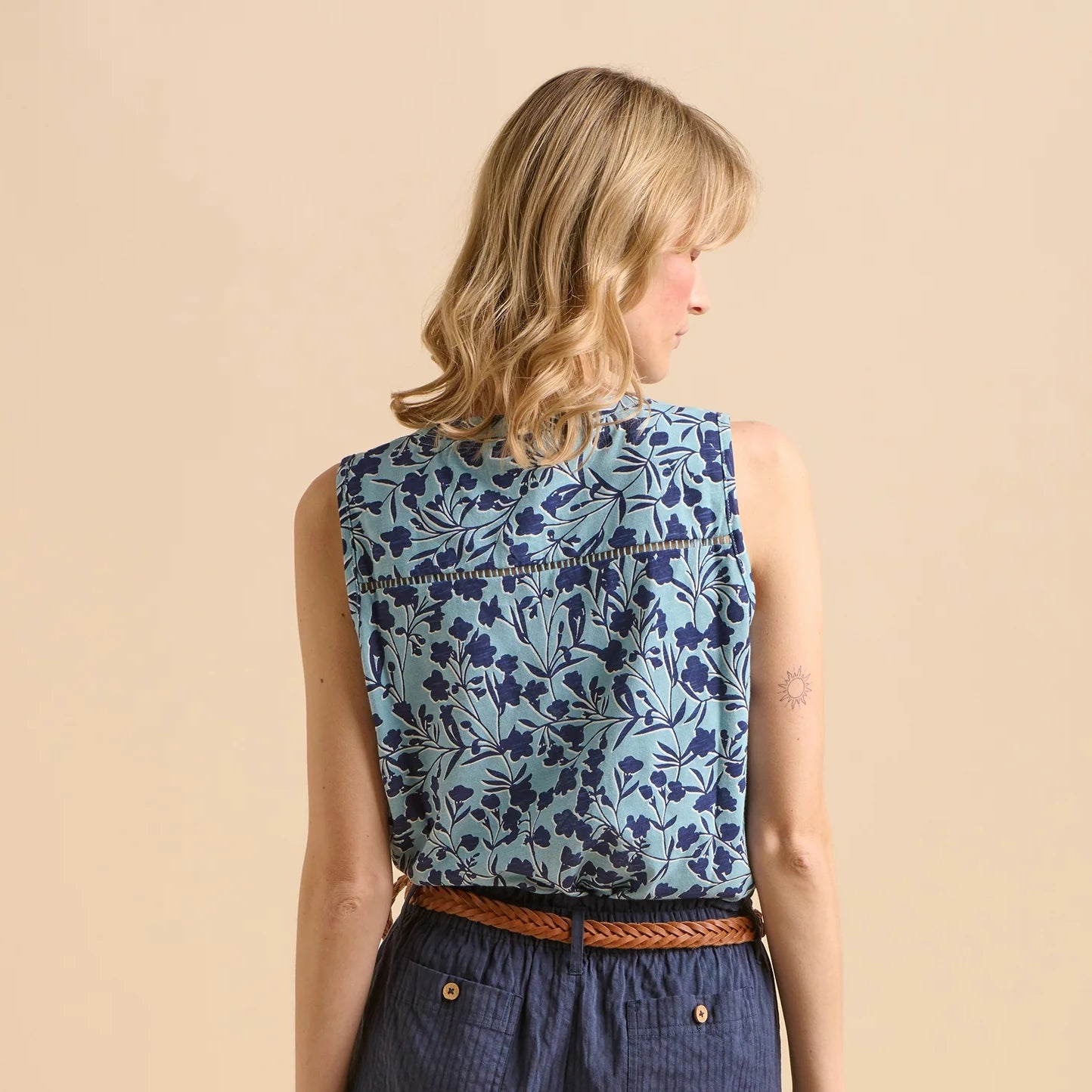 Back view of a woman wearing a Brakeburn sleeveless blue floral vest top on a beige background