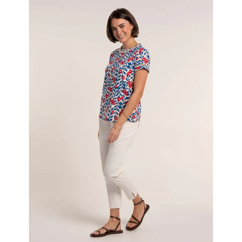 Side view of a woman wearing a Brakeburn short sleeve Clara t-shirt with a blue and red floral pattern and lace trim around the neckline and sleeves with white cut-off trousers.