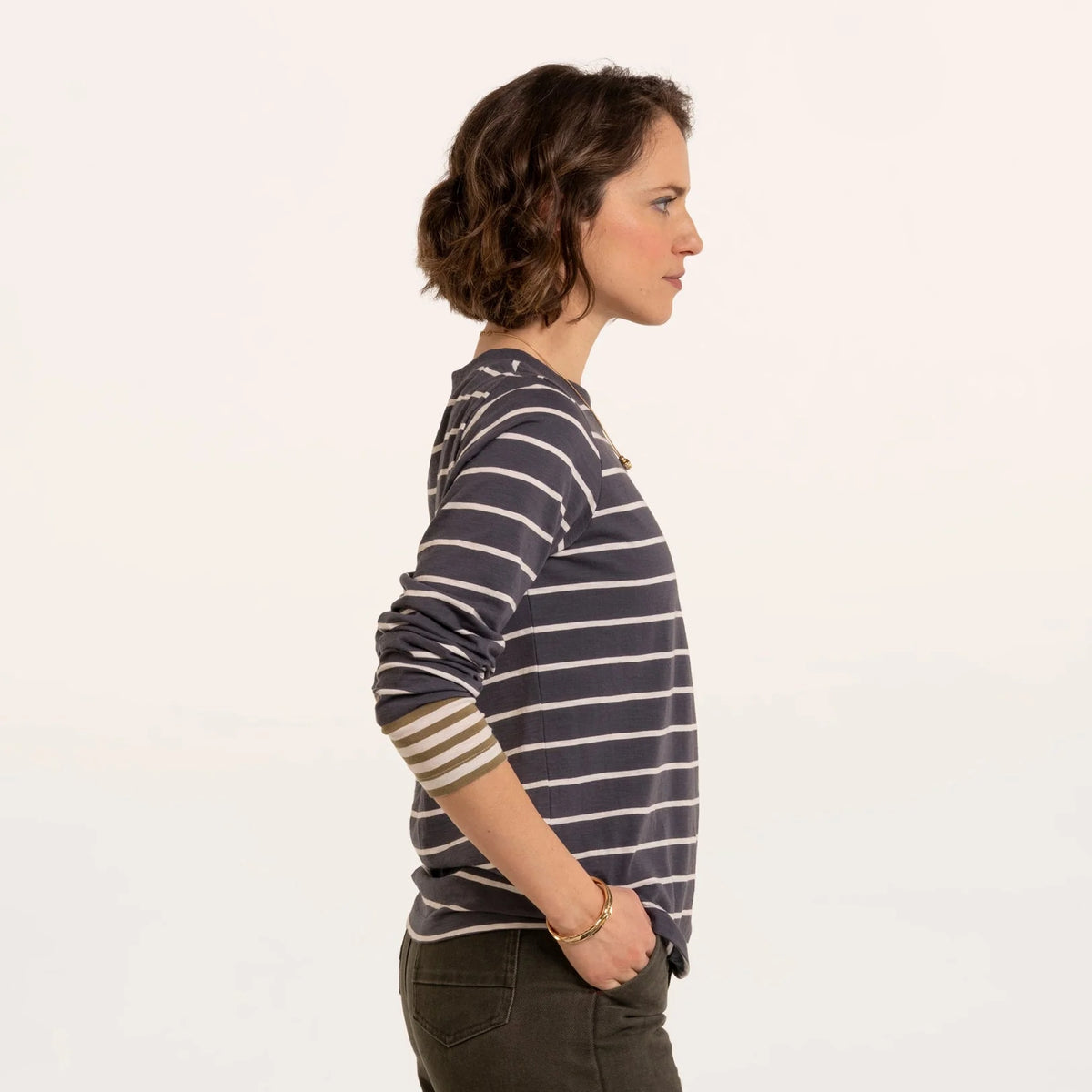 Side view of a woman wearing a Brakeburn long sleeve Exbury t-shirt in light navy with white stripes and contrasting mustard stripe cuffs.