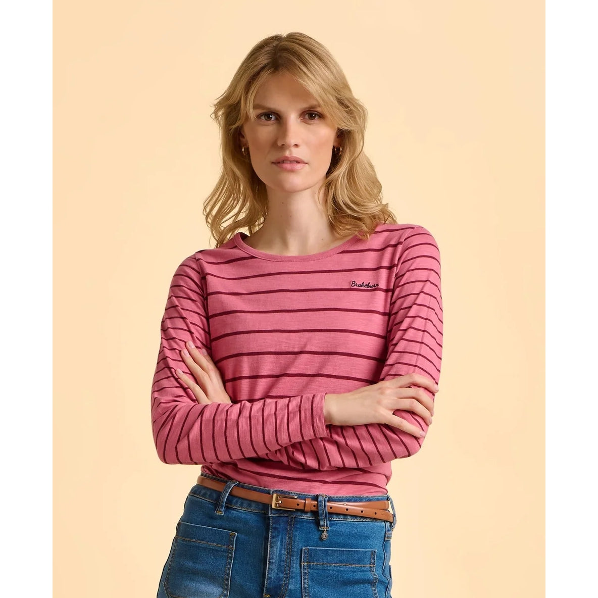 Woman wearing a pink striped t-shirt with a brand logo on a beige background