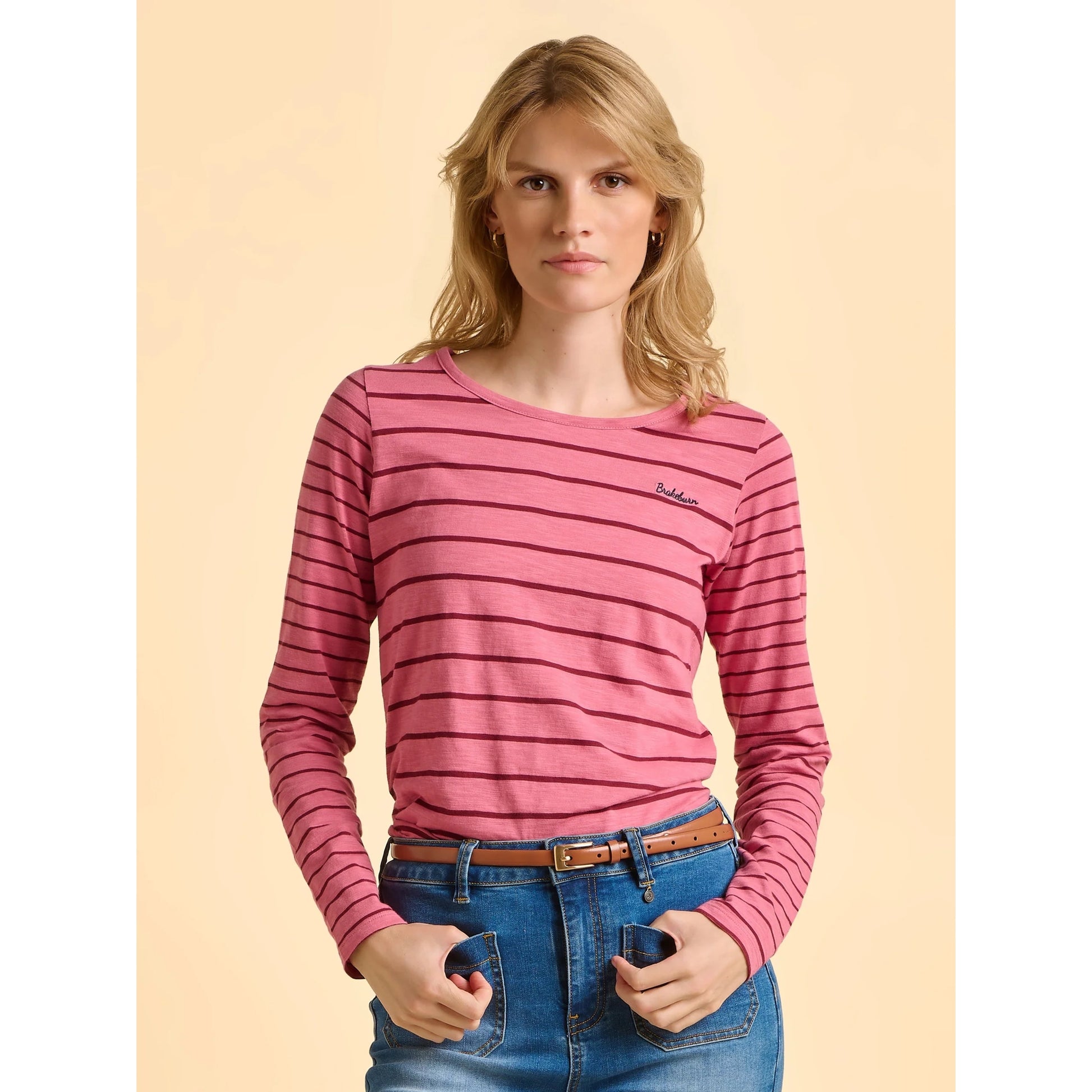 Woman wearing a pink striped long-sleeve shirt against a beige background