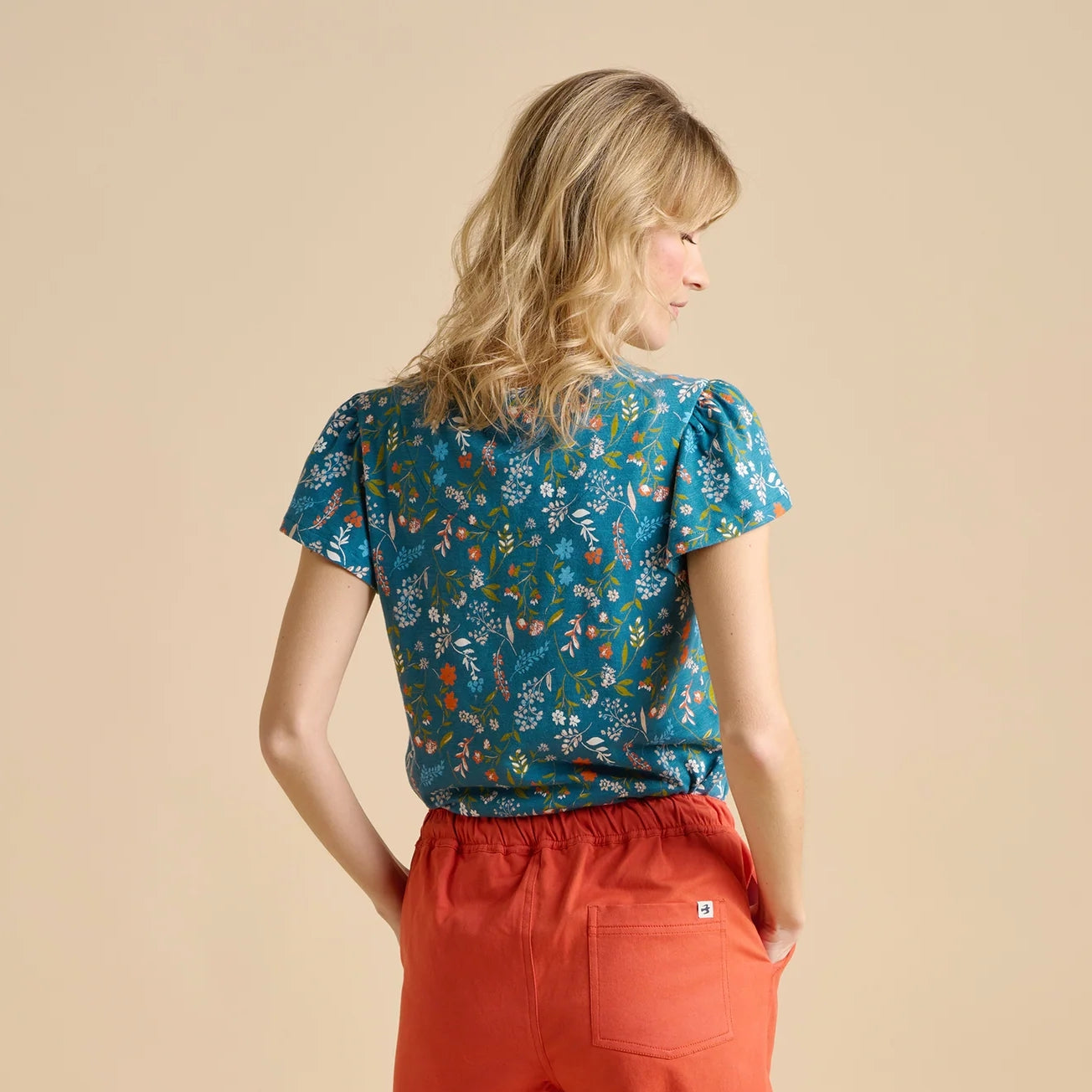 Woman wearing a teal Brakeburn meadow floral t-shirt and red pants on a beige background