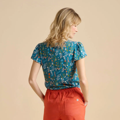 Woman wearing a teal Brakeburn meadow floral t-shirt and red pants on a beige background