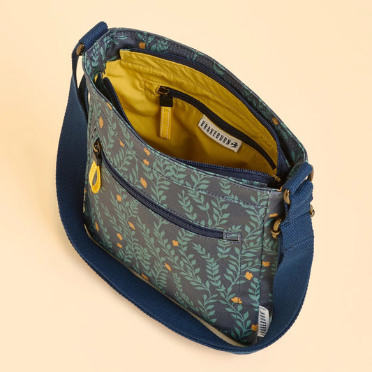 Floral leaf patterned Brakeburn Twilight Leaves Cross Body bag with a visible brand logo and zip pockets on a beige background