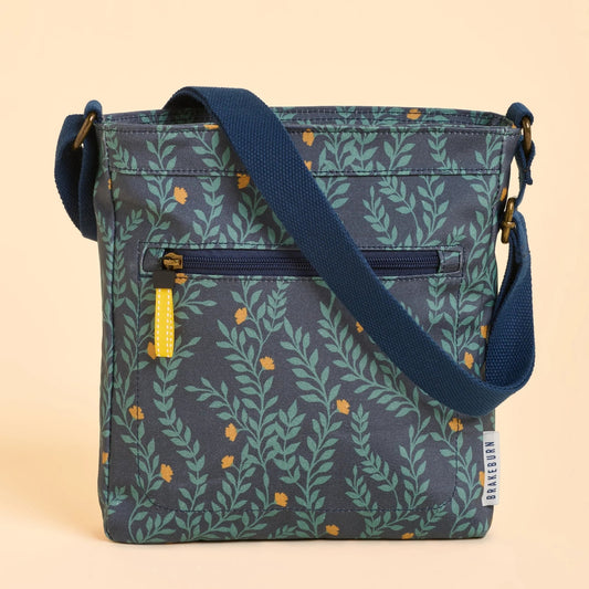 Front view of a Brakeburn Twilight Leaves floral leaf patterned cross body bag with a blue strap on a beige background