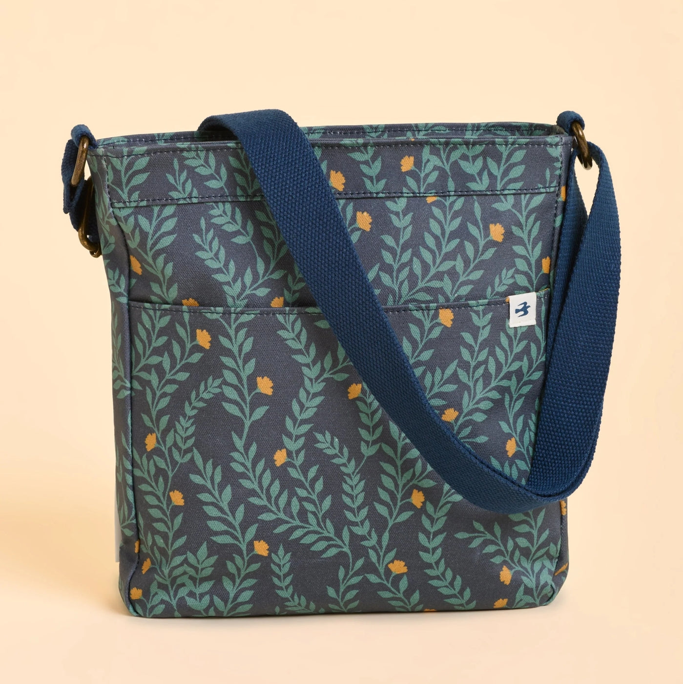 Back view of a Brakeburn Twilight Leaves cross body bag with floral leaf pattern and a blue strap on a beige background 