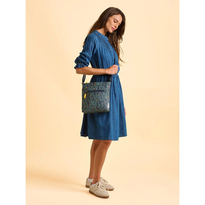 Woman in a blue dress wearing a Brakeburn Twilight Leaves cross body bag against a beige background