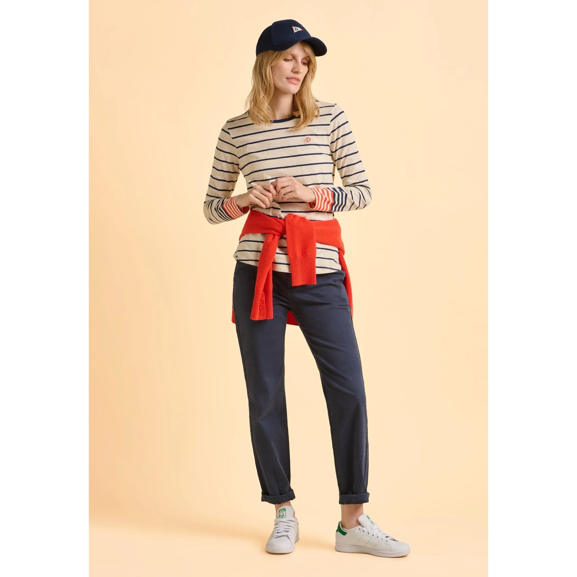Woman wearing a striped Brakeburn cream Knoll t-shirt and navy pants on a beige background