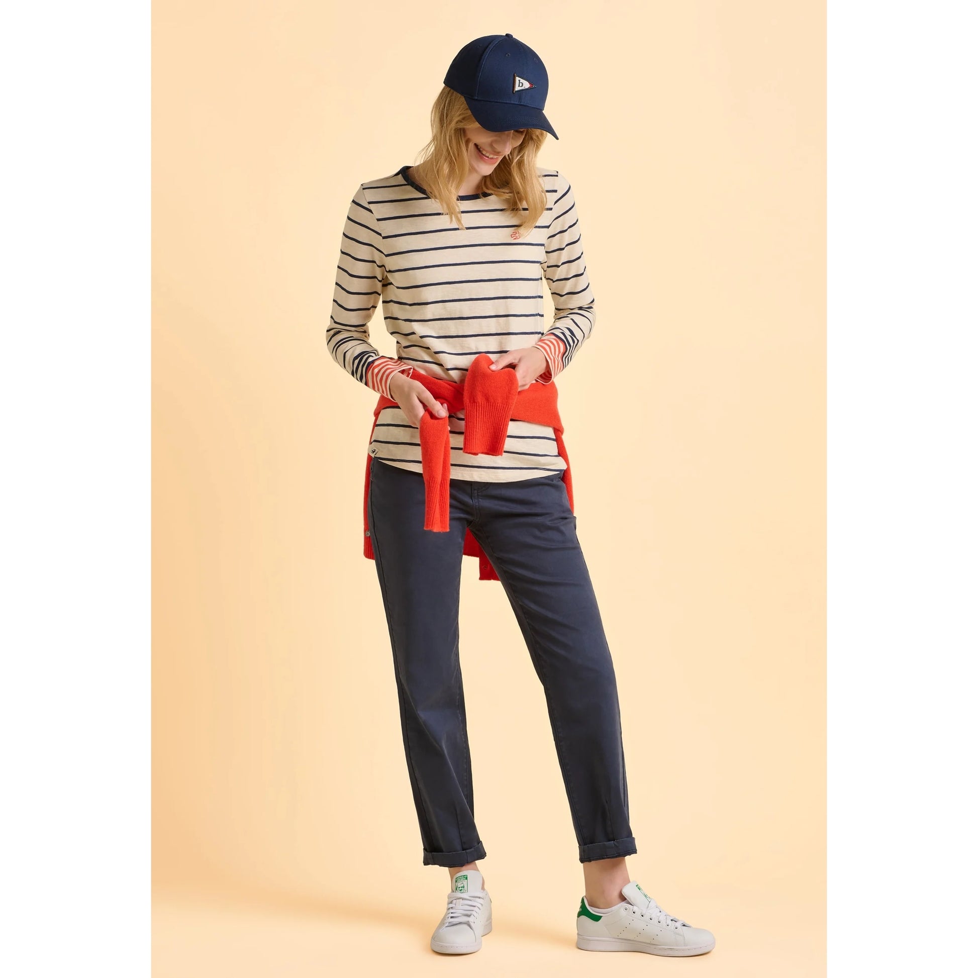 Woman wearing a Brakeburn long sleeve striped Knoll t-shirt and navy trousers on a beige background