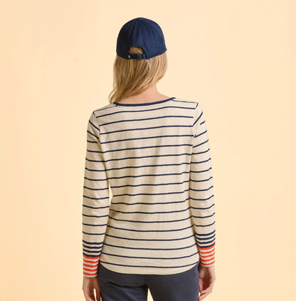 Back view of a woman wearing a striped Brakeburn long-sleeve Knoll t-shirt and navy cap on a beige background