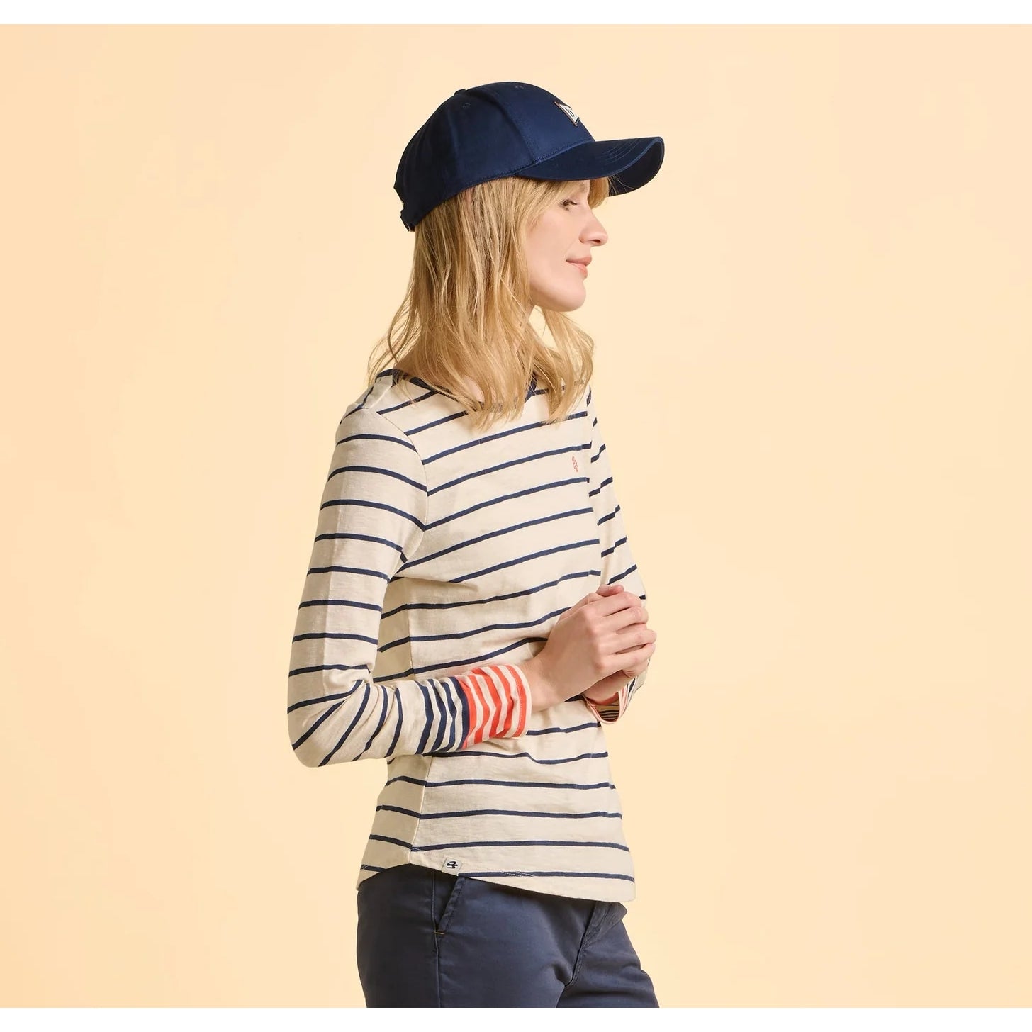 Woman wearing a navy cap and striped Brakeburn Knoll long sleeve t-shirt in cream on a beige background