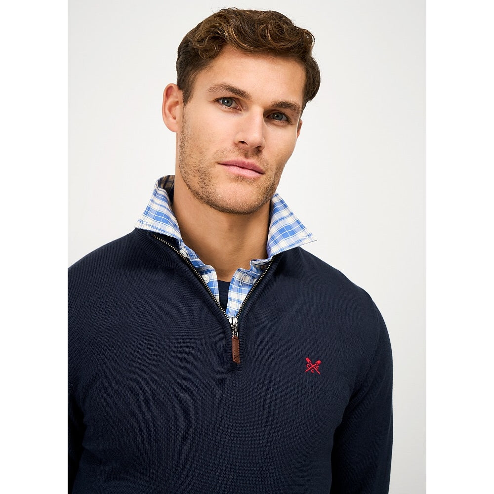 Close-upp view of a man wearing a Crew Clothing 1/4 zip classic knitted jumper in Heritage Navy with small red crossed oars logo on the chest