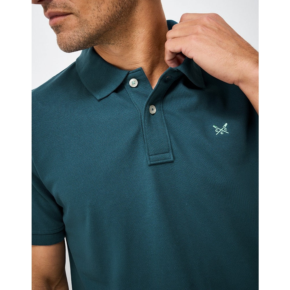 Close-up view of a mens Crew Clothing short sleeve classic pique polo shirt in Teal with small crossed oars logo on the chest