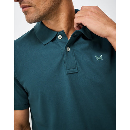 Close-up view of a mens Crew Clothing short sleeve classic pique polo shirt in Teal with small crossed oars logo on the chest