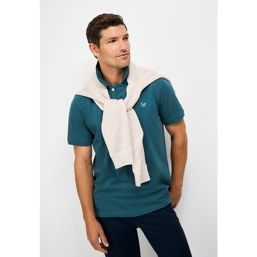 Front view of a man wearing a Crew Clothing short sleeve classic pique polo shirt in Teal with small crossed oars logo on the chest